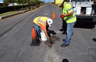 Asphalt repair patching pothole on road in Honolulu by two men